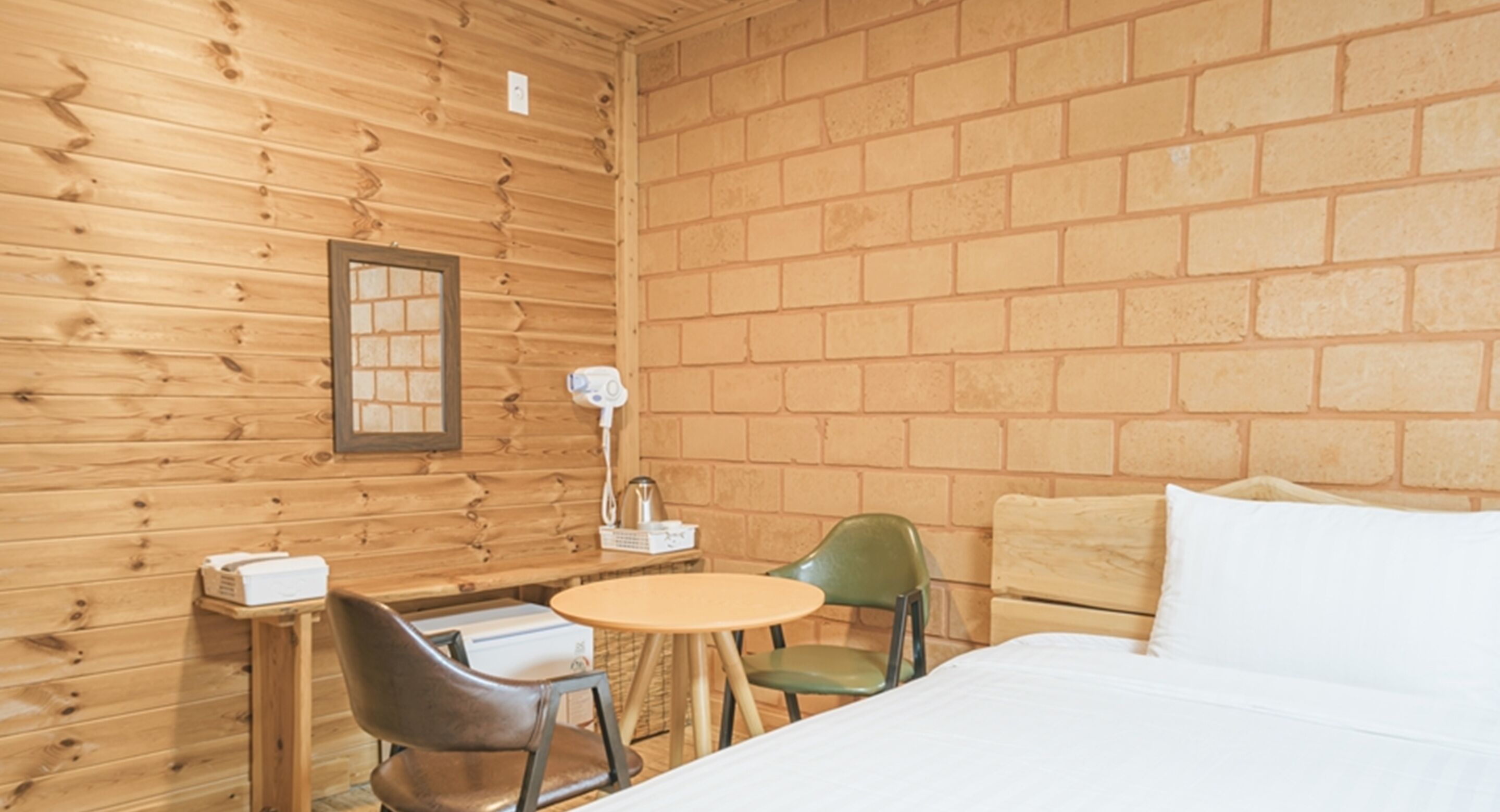 A wooden cabin room with a bed, a small table, two chairs, and a brick wall.