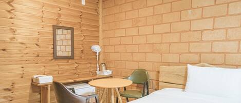 Una habitación de cabaña de madera con una cama, una mesita pequeña, dos sillas y una pared de ladrillo.