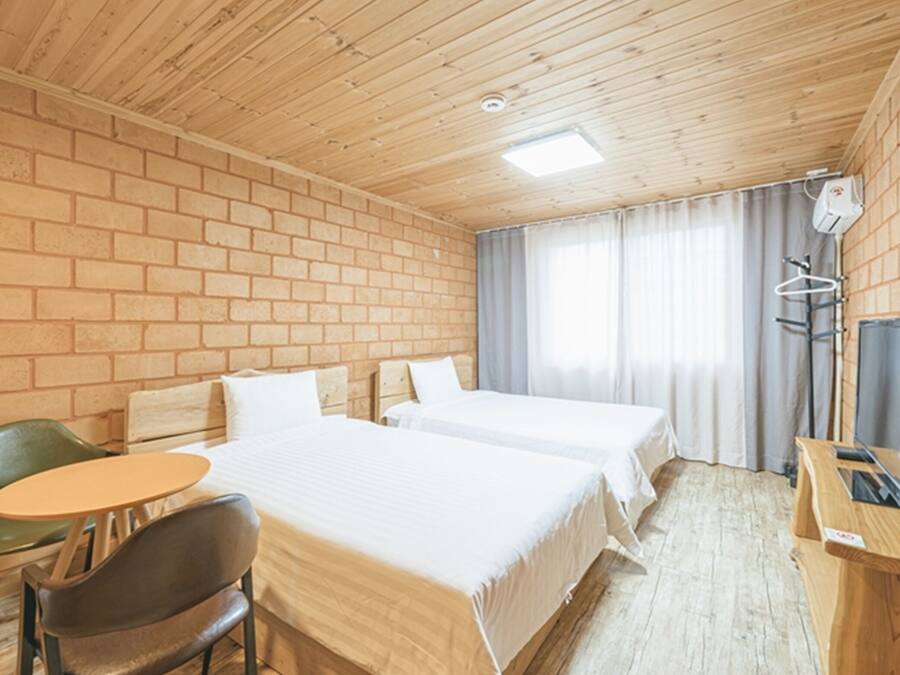 Une chambre d’hôtel avec deux lits, une petite table, une chaise, un bureau avec un ordinateur et une télévision.