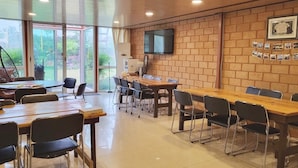 A conference room with a long table and chairs, a television on the wall, and a brick wall with photos. - Jeju Healing Resort (Jeju City)