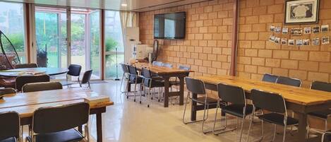 A conference room with a long table and chairs, a television on the wall, and a brick wall with photos.