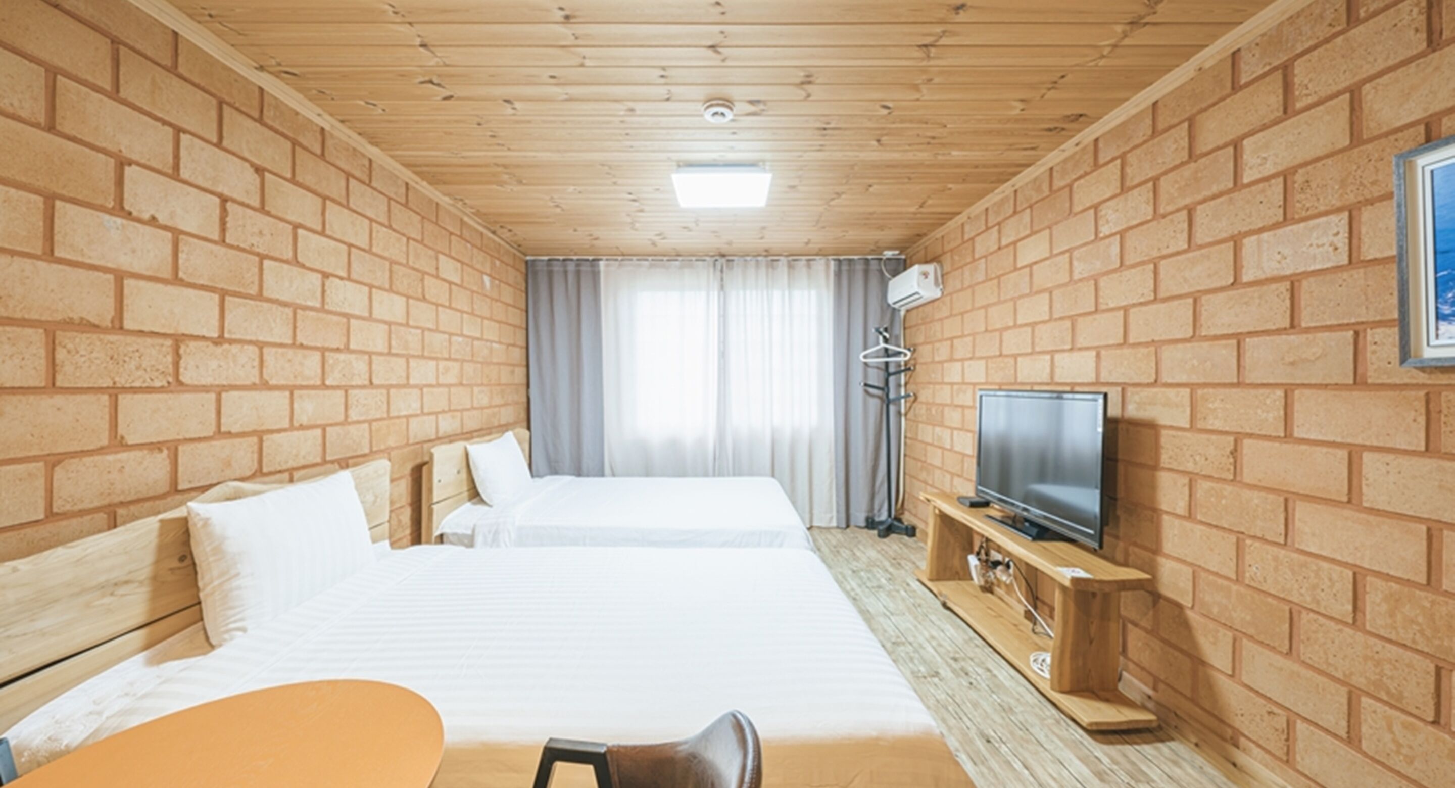 A hotel room with two beds, a TV, a desk, and a window with curtains.