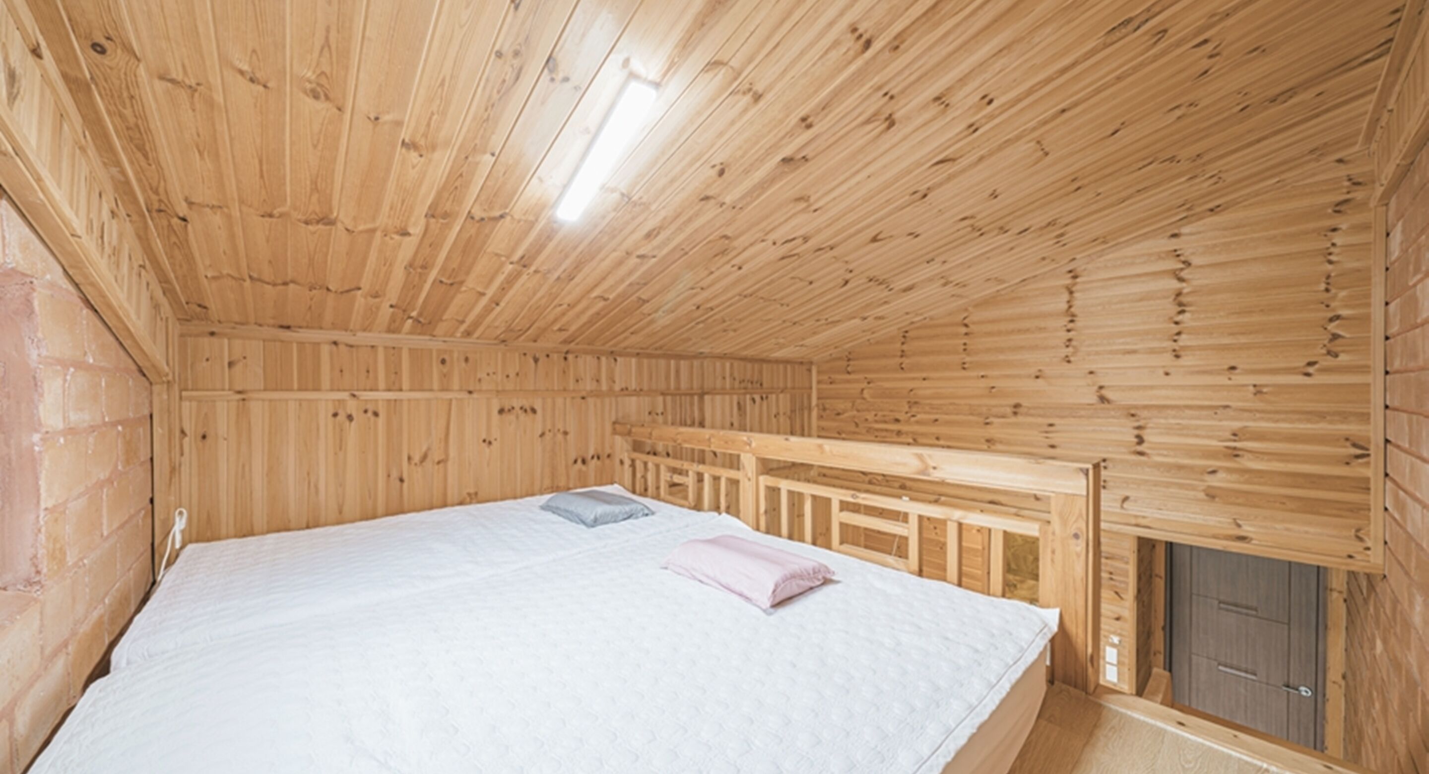 A wooden cabin bedroom with a bed, a bench, and a door.