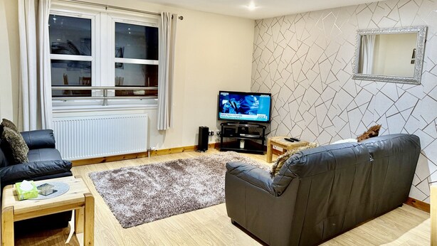 A modern living room with a grey sofa, a wooden coffee table, a TV on a stand, and a patterned rug.