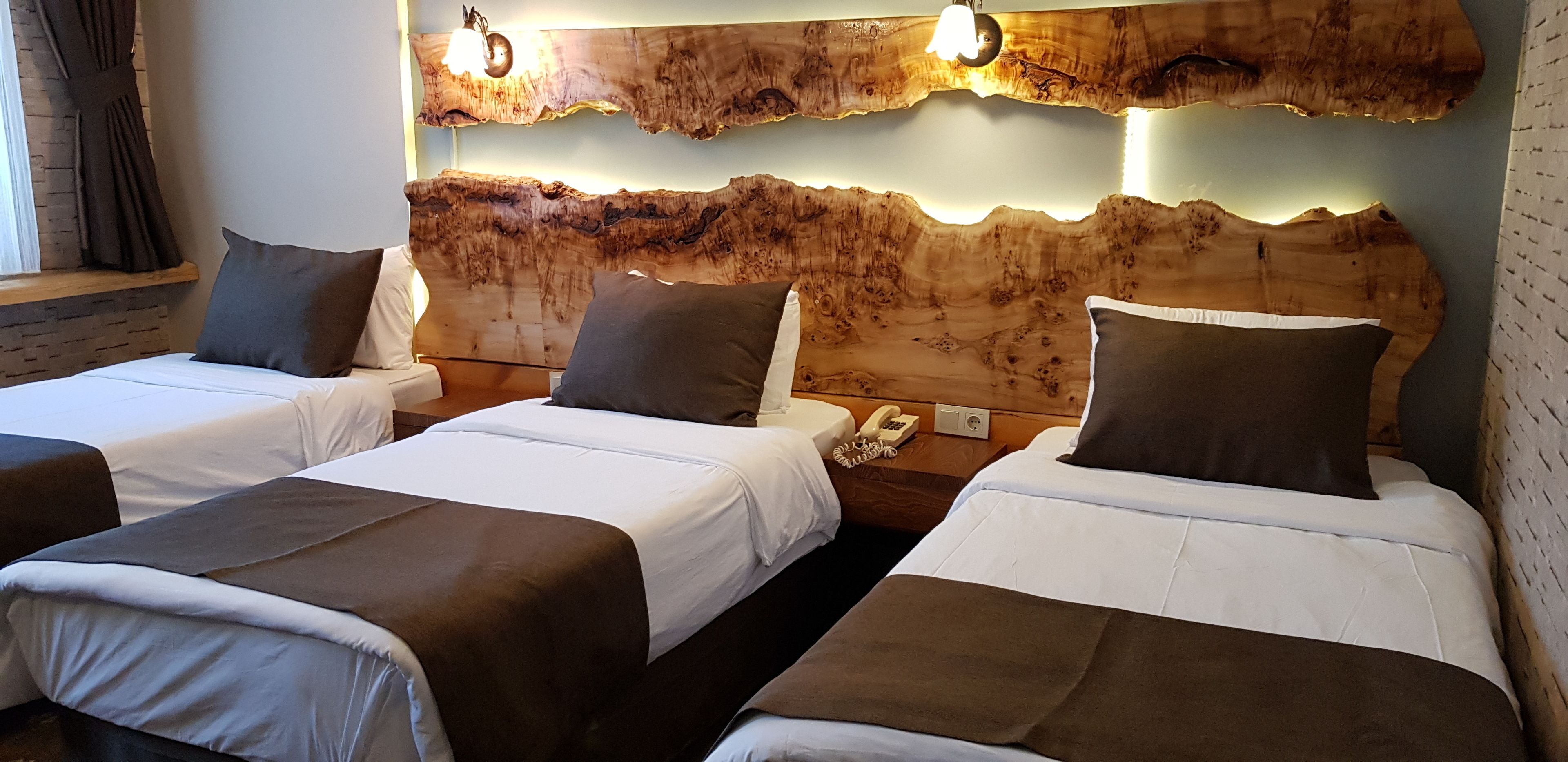 A hotel room with two beds, a wooden headboard, bedside lamps, a telephone, and a window with curtains.