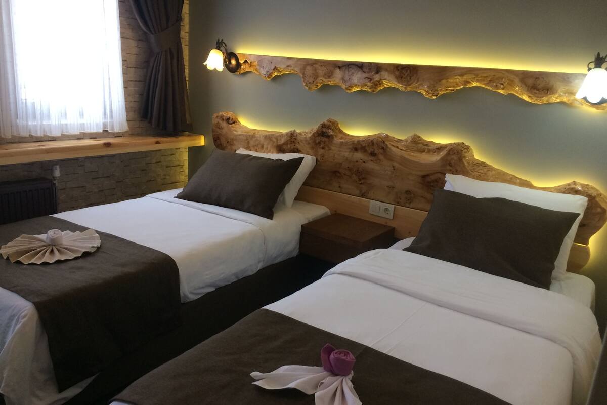 Deux lits simples avec du linge de lit blanc et des têtes de lit marron, une décoration murale en bois et une fenêtre avec des rideaux.