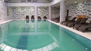 Una piscina interior con un muro de azulejos con diseños geométricos y una fila de tumbonas a lo largo de un lado.
