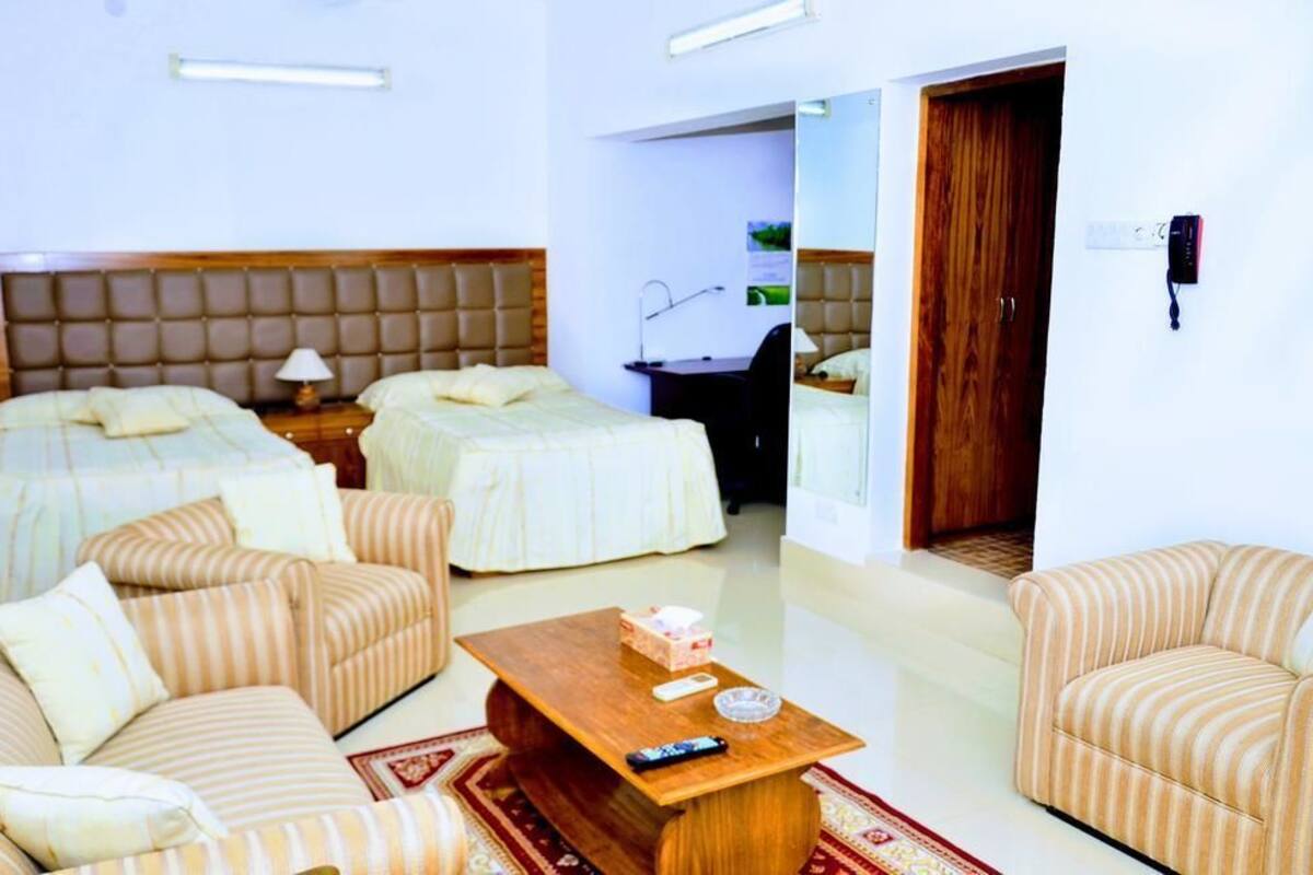 Une chambre d’hôtel avec deux lits, un canapé, une table basse et un bureau avec une lampe.