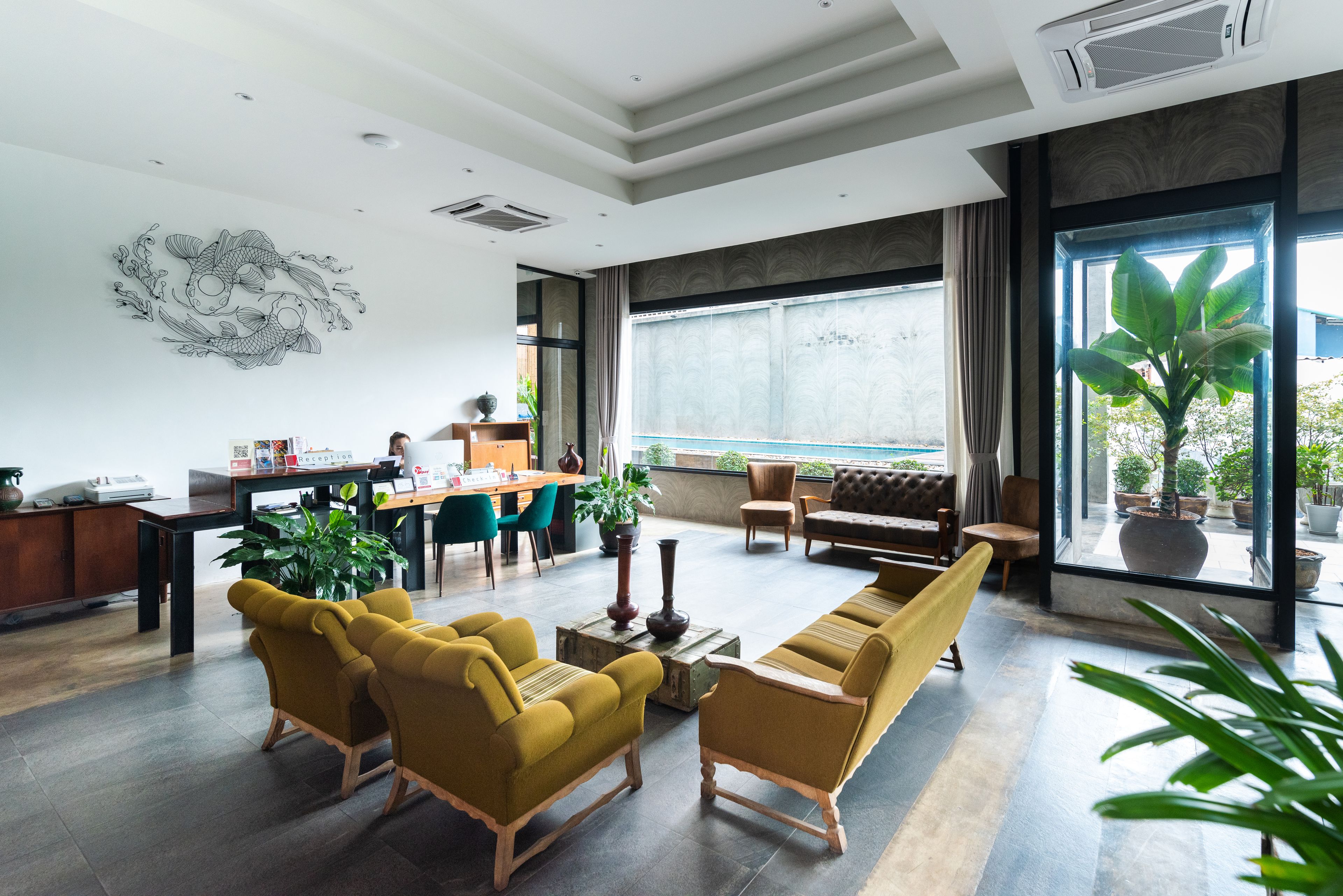 A modern hotel lobby with a seating area, a reception desk, and large windows offering a view of the outdoors.
