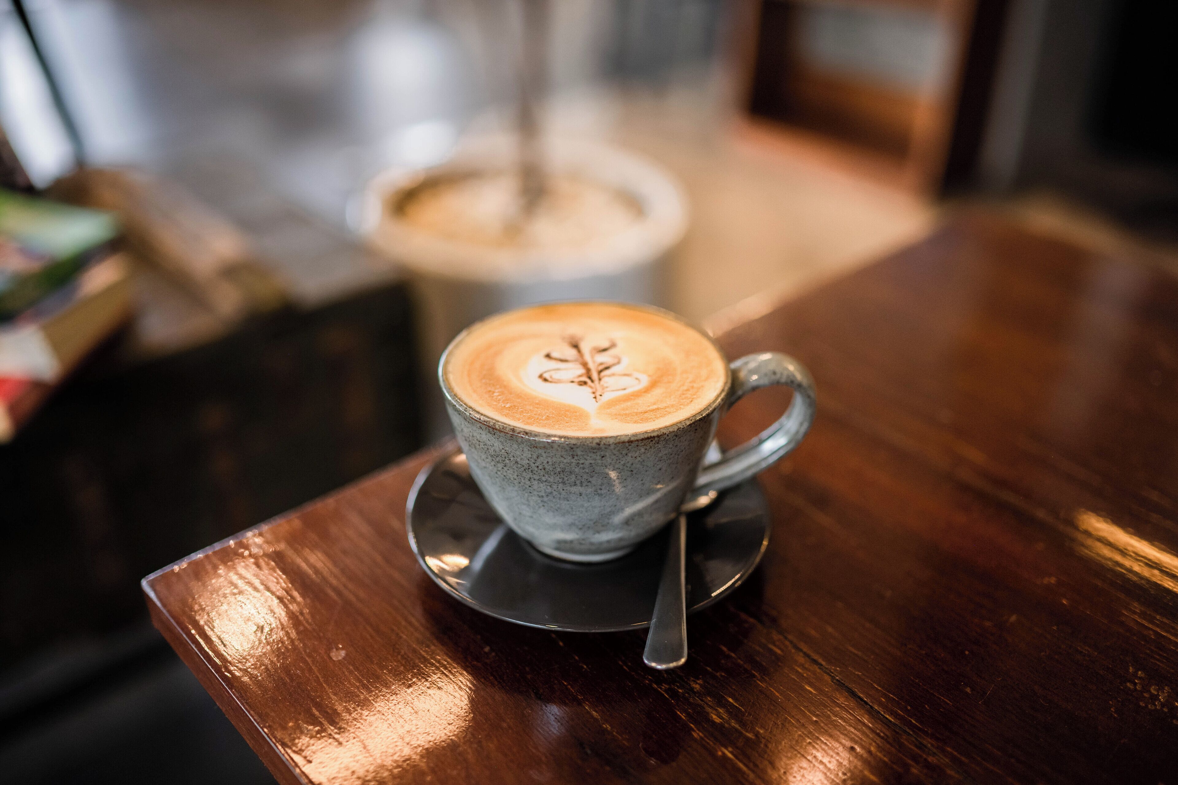 A cup of coffee with latte art on a saucer on a wooden table.