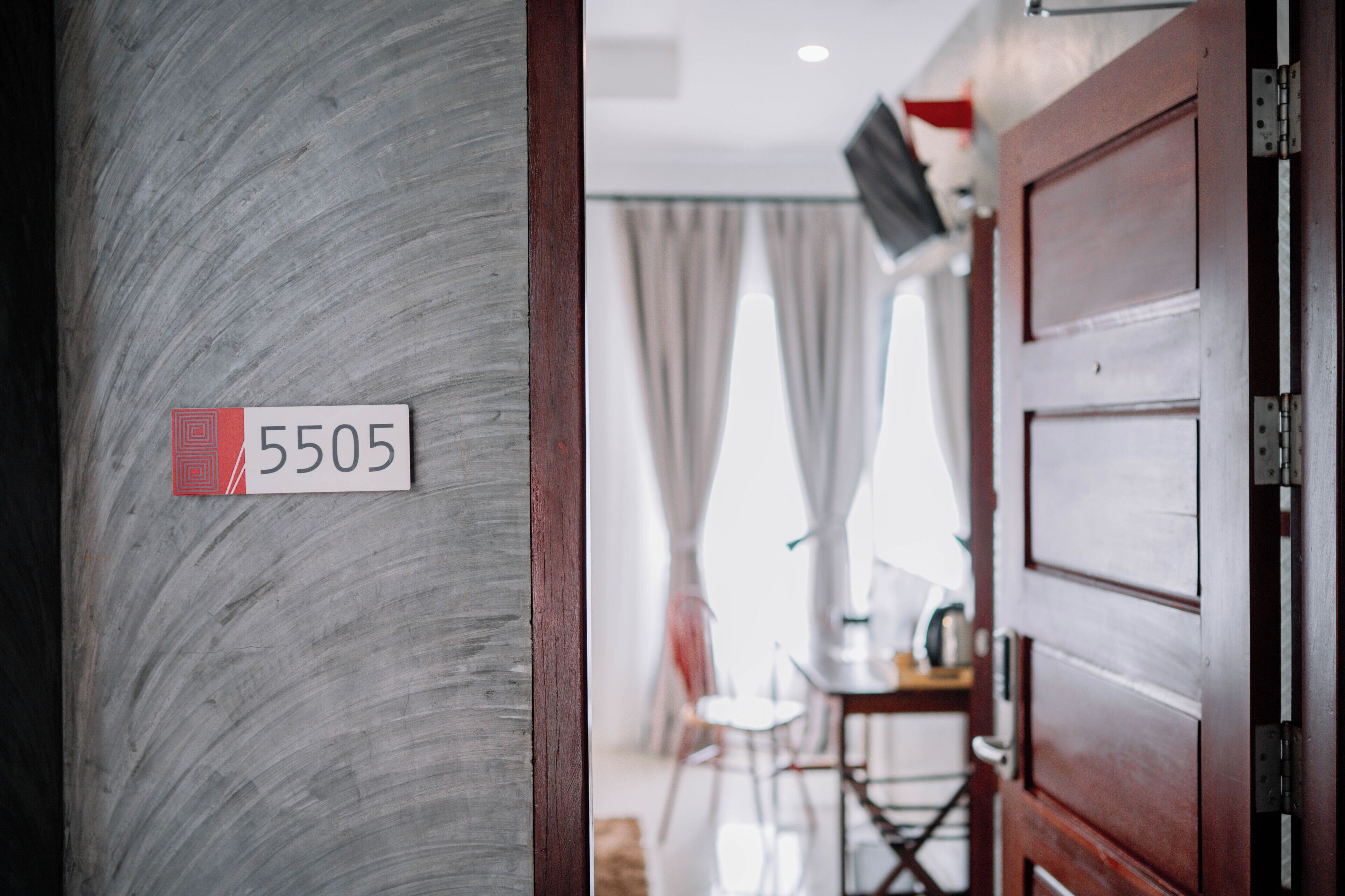 A hotel room with a wooden door, a number sign, and a glimpse of a dining area with a table and chairs.