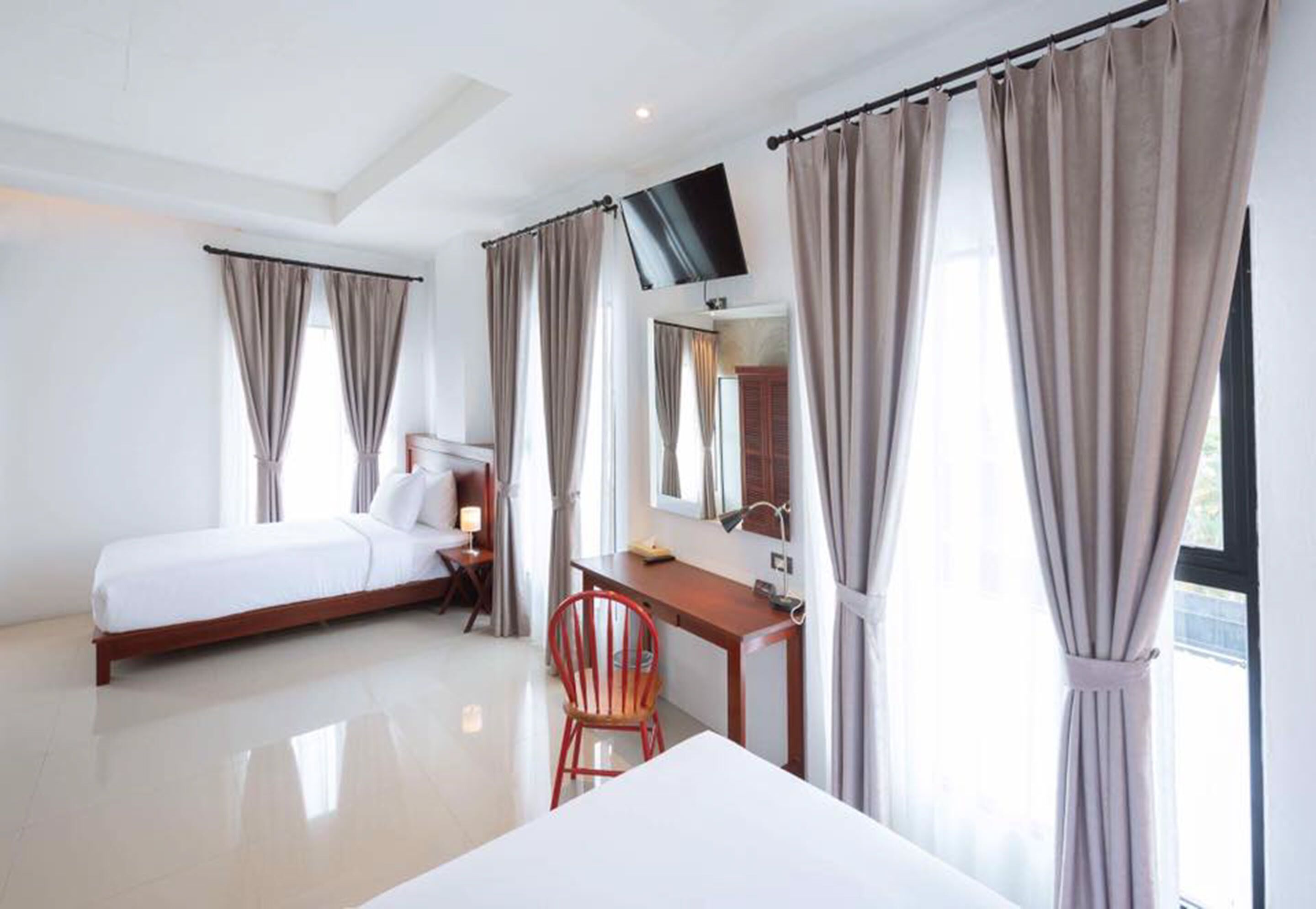 Una habitación de hotel con cama, escritorio, silla, televisor y cortinas.