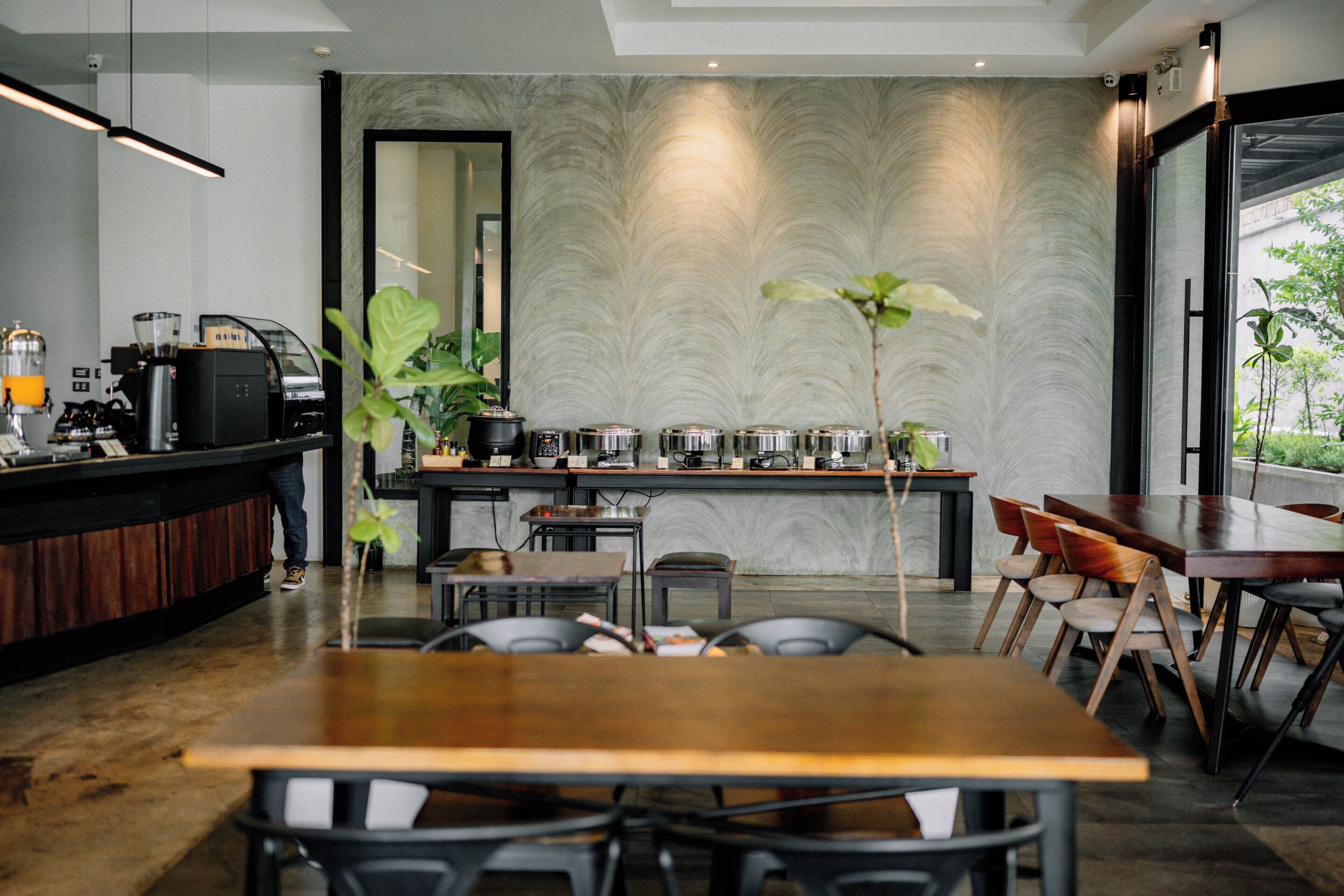 A modern cafe with a wooden table and chairs, a counter with a coffee machine, and a patterned wall.