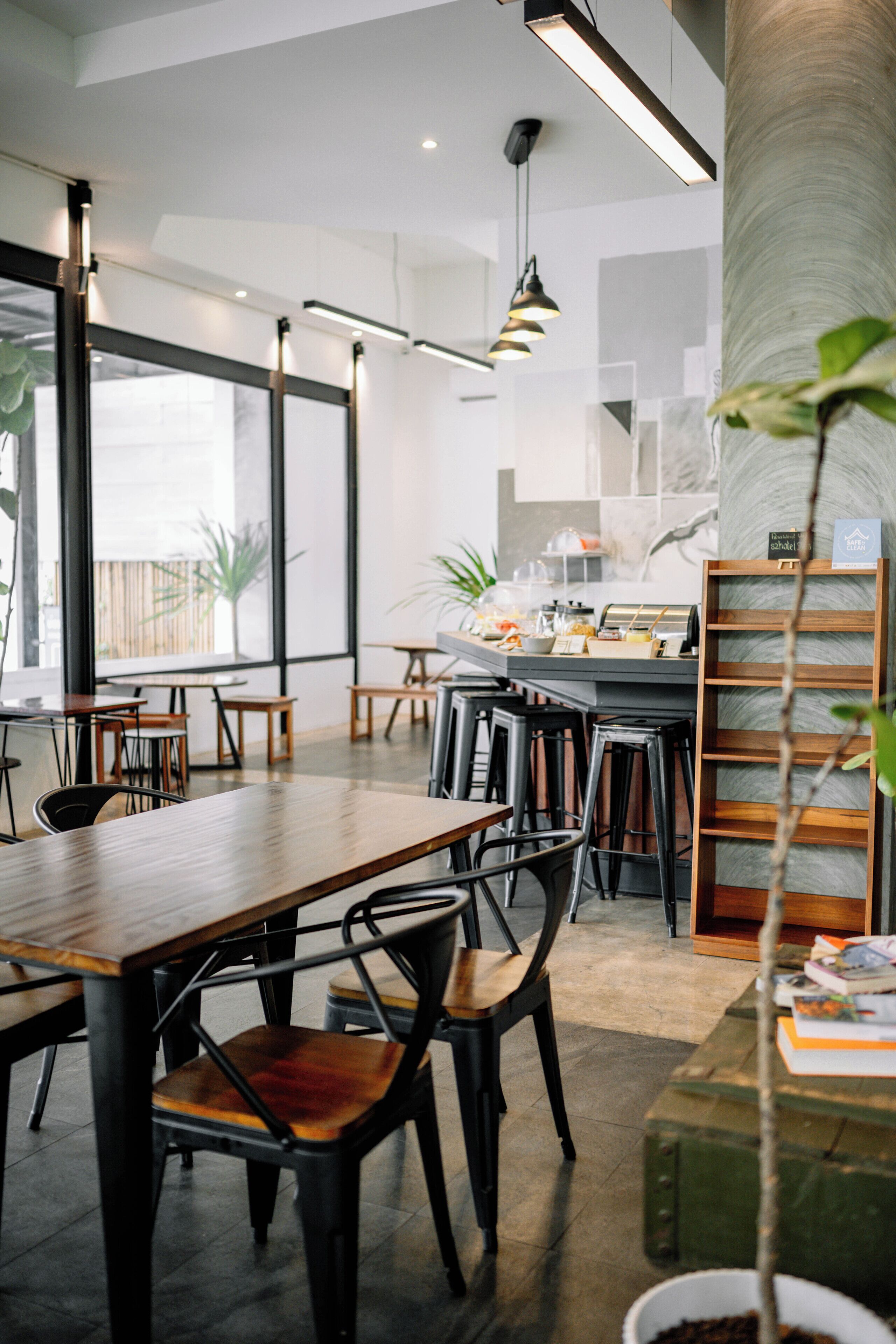 A modern cafe with wooden tables and chairs, large windows, and a counter with a menu.