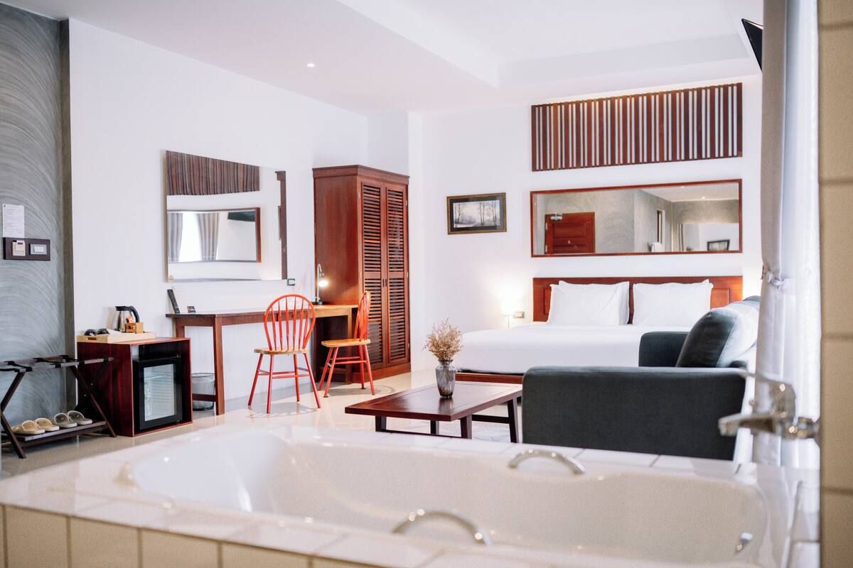 Habitación de hotel moderna con una cama grande, un escritorio con silla, un televisor pequeño y una bañera.
