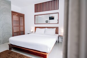 Un dormitorio moderno con una cama grande, cabecera de madera, televisor montado en la pared y un espejo amplio.