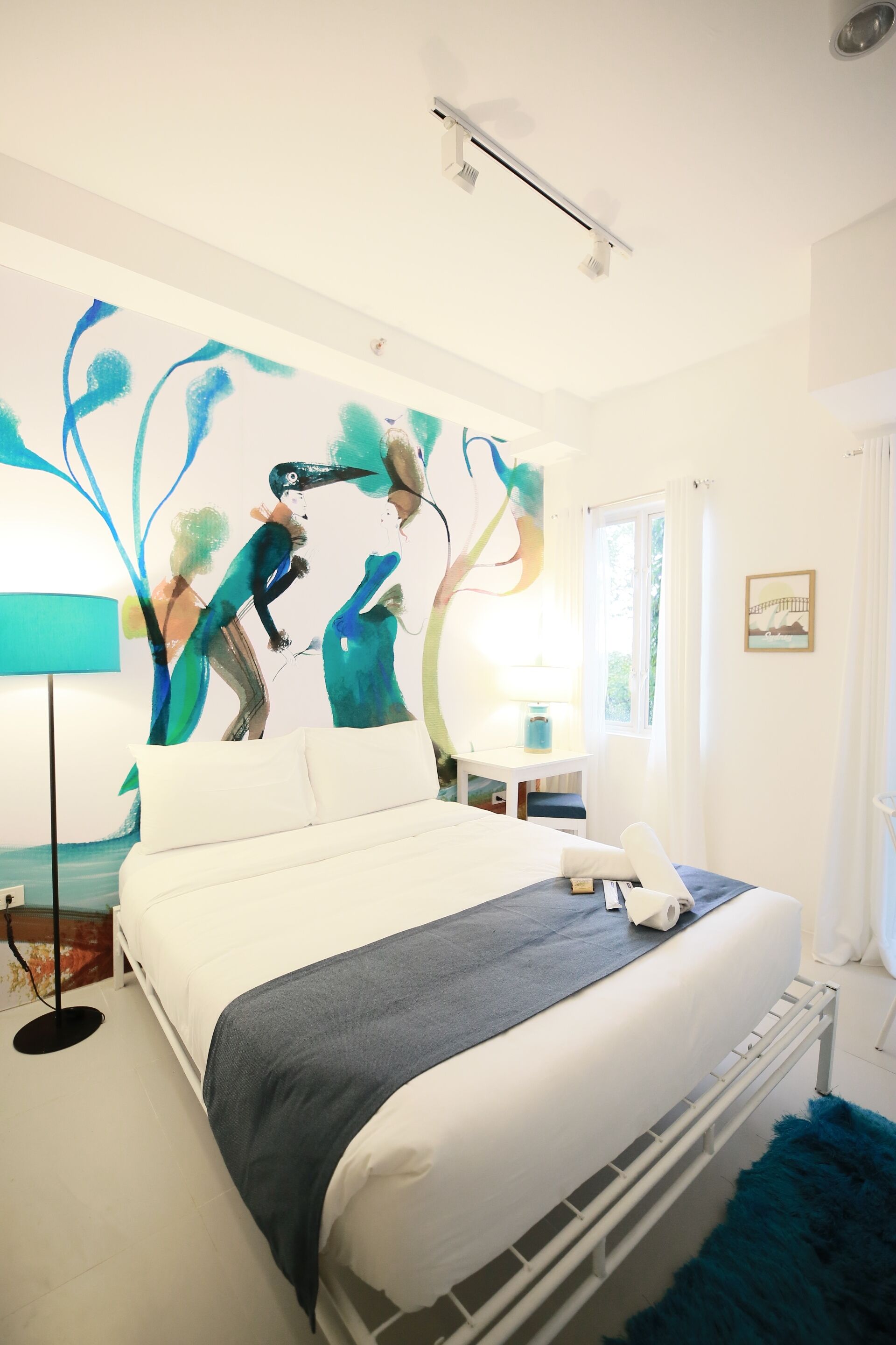 A modern bedroom with a large bed, a desk, and a wall painting.