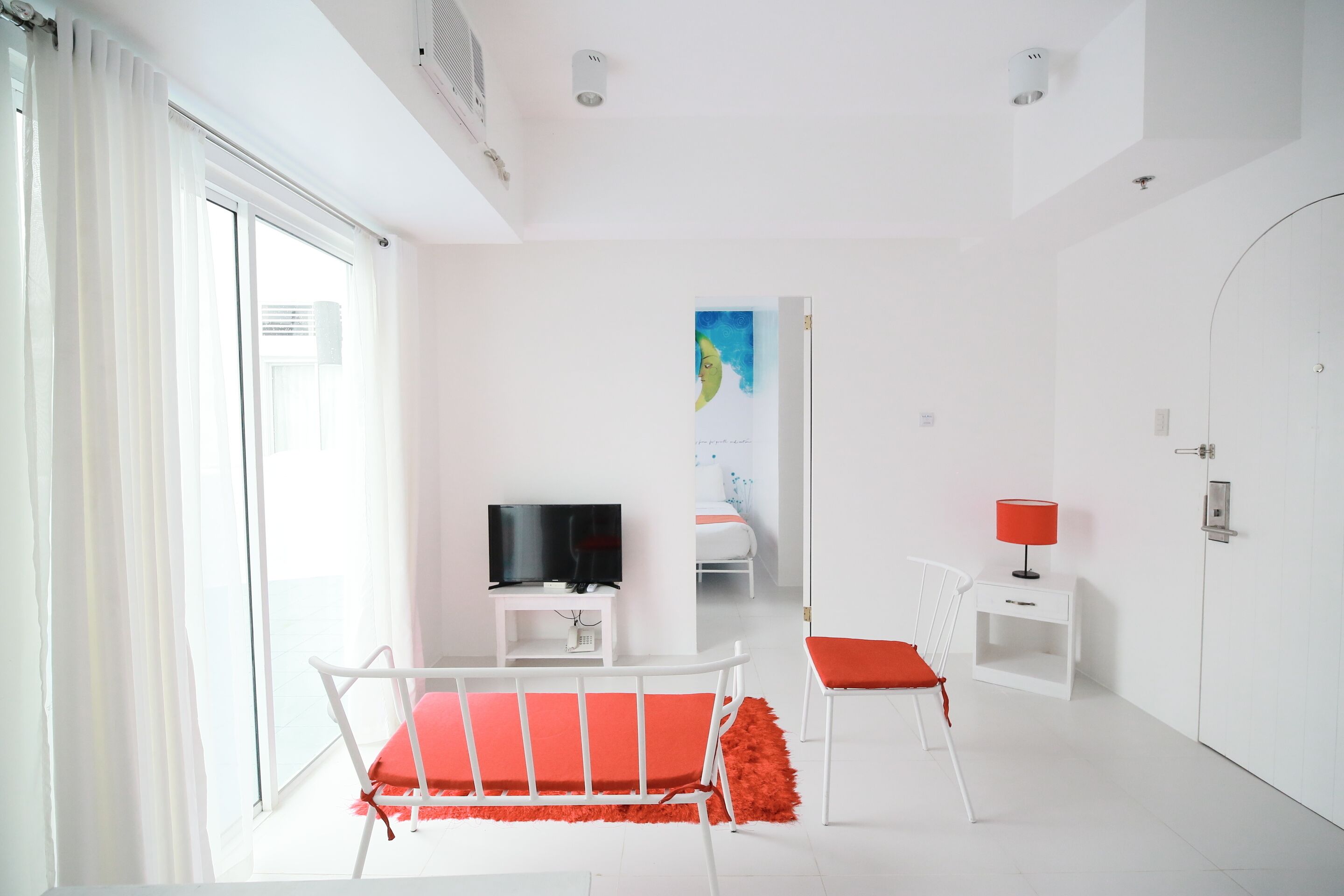 A bright, white room with a bed, a TV, a small table, and a chair.