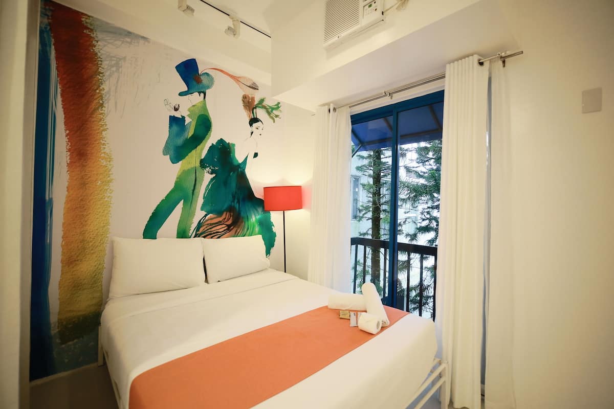 Hotelkamer met een groot bed, een rode lamp, een raam met uitzicht op bomen en een schilderij aan de muur.