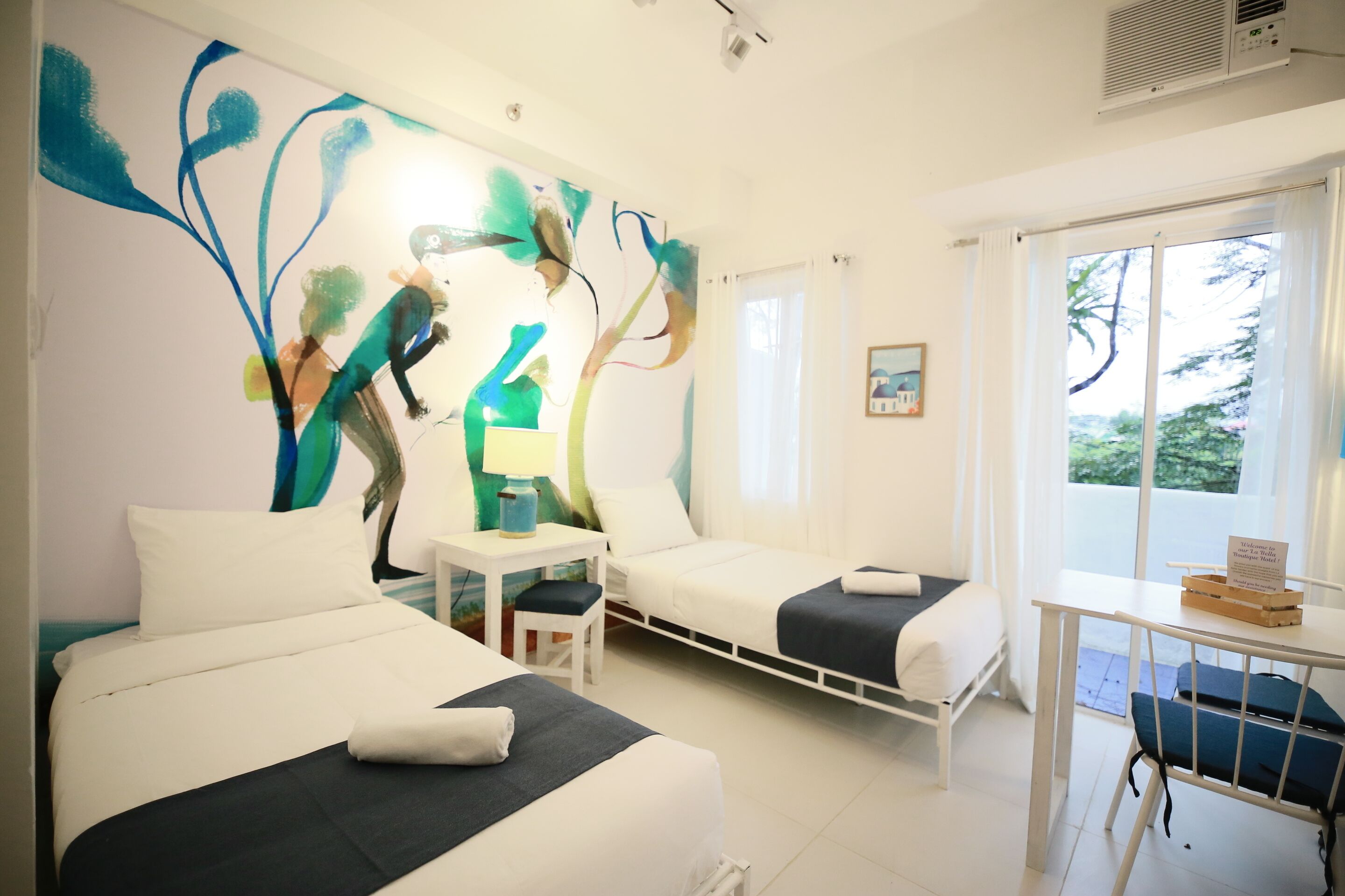 Habitación de hotel con dos camas, una mesita y un ventanal con vista a árboles.
