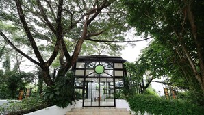 Uma entrada coberta com porta de vidro, cercada por vegetação exuberante e uma parede branca.