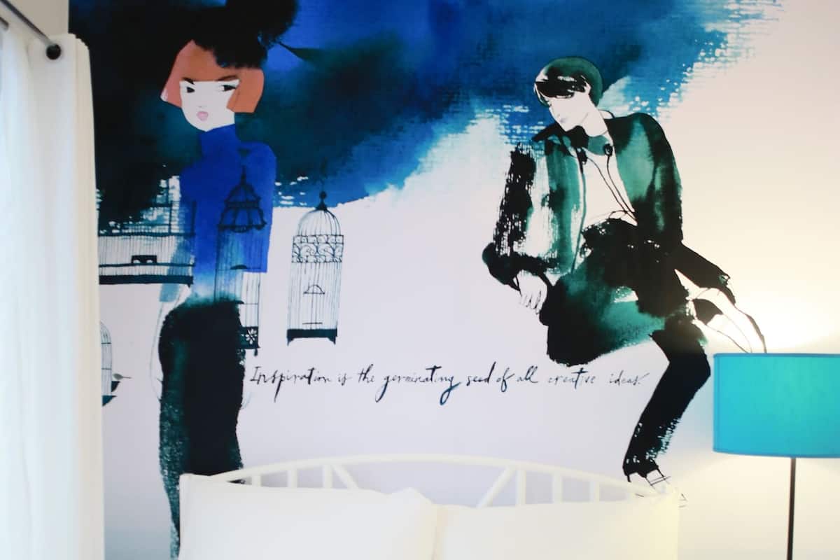 Een slaapkamer met een bed, een lamp en een groot abstract schilderij aan de muur.