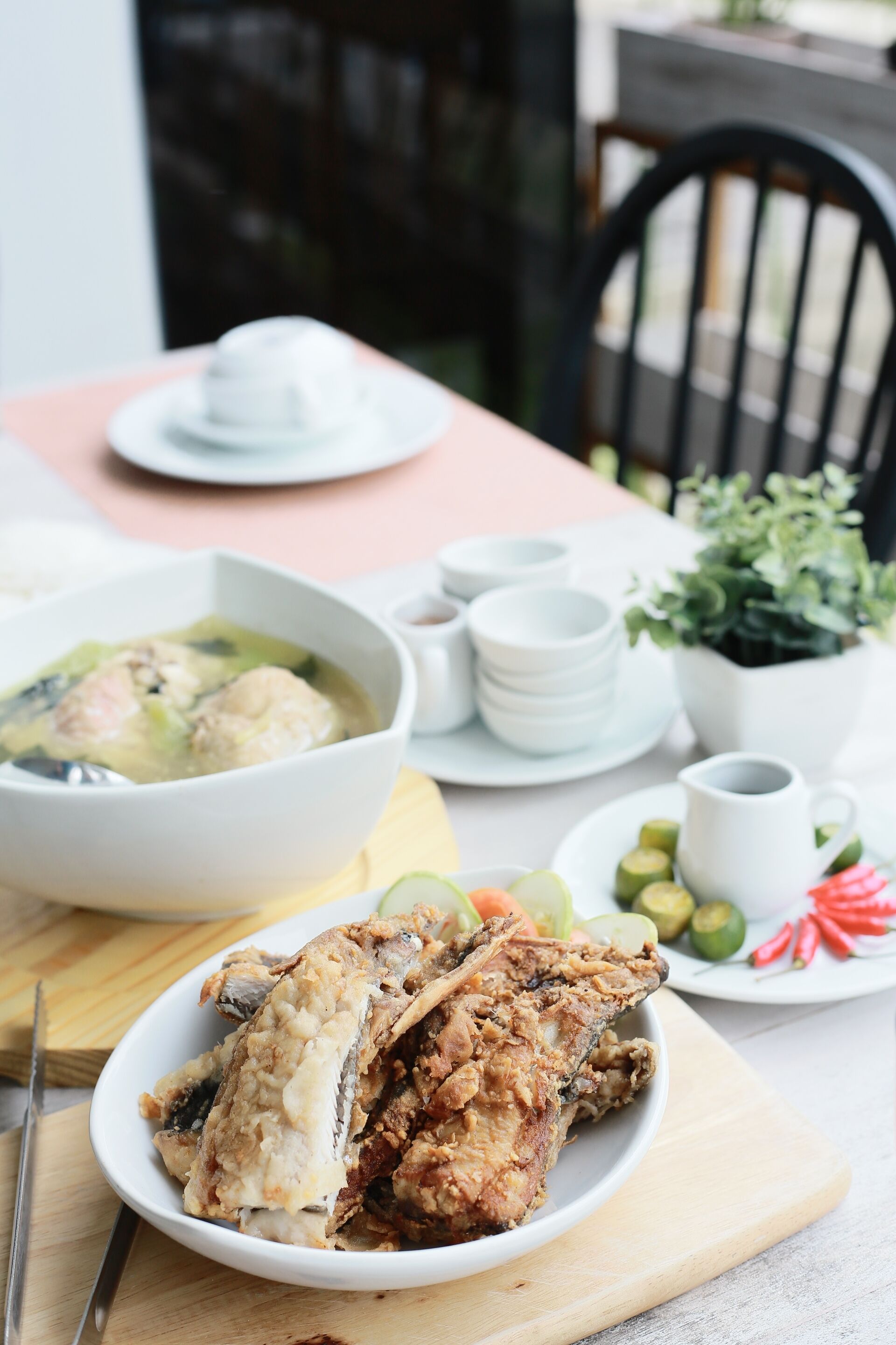 A dining table with a bowl of soup, a plate of fried chicken, and various condiments.