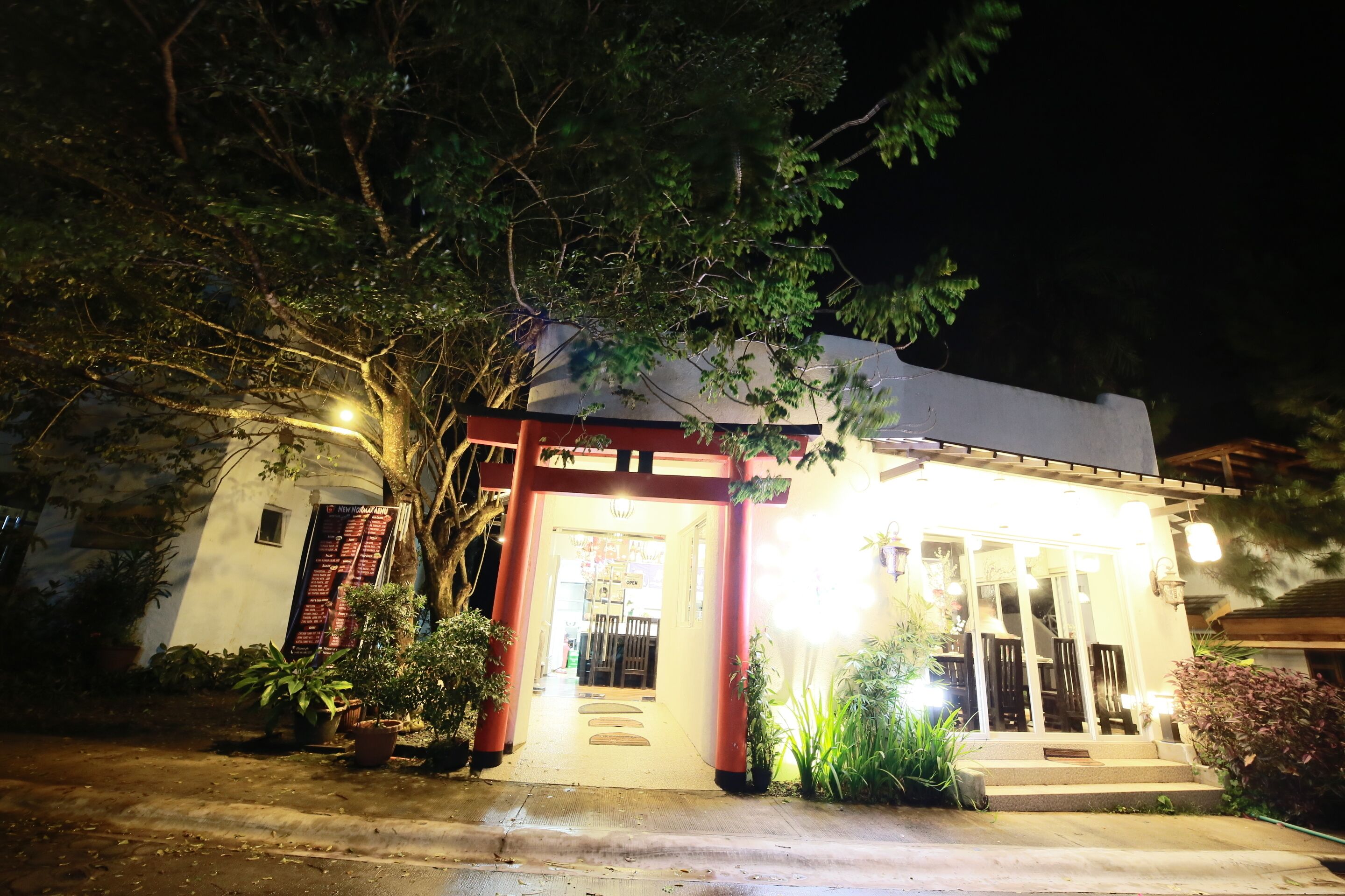 A building with a covered entrance, potted plants, and a pathway leading to the door.