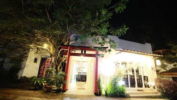 A building with a covered entrance, potted plants, and a pathway leading to the door.