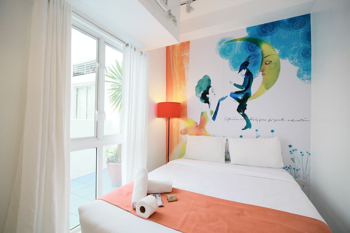Een hotelkamer met een bed, een groot raam met gordijnen, een wanddecoratie en een rode lamp.