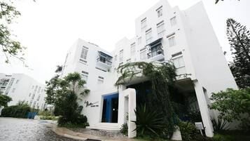 Un edificio moderno blanco con una entrada azul, rodeado de vegetación y un camino adoquinado.