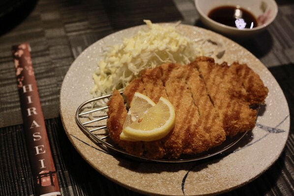 A plate with a breaded cutlet, lemon slice, and shredded cabbage, accompanied by a small bowl of sauce. - La Bella Boutique Hotel (Tagaytay)