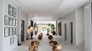 Um saguão de hotel moderno com uma recepção central, obras de arte emolduradas nas paredes e esculturas de madeira únicas no chão.