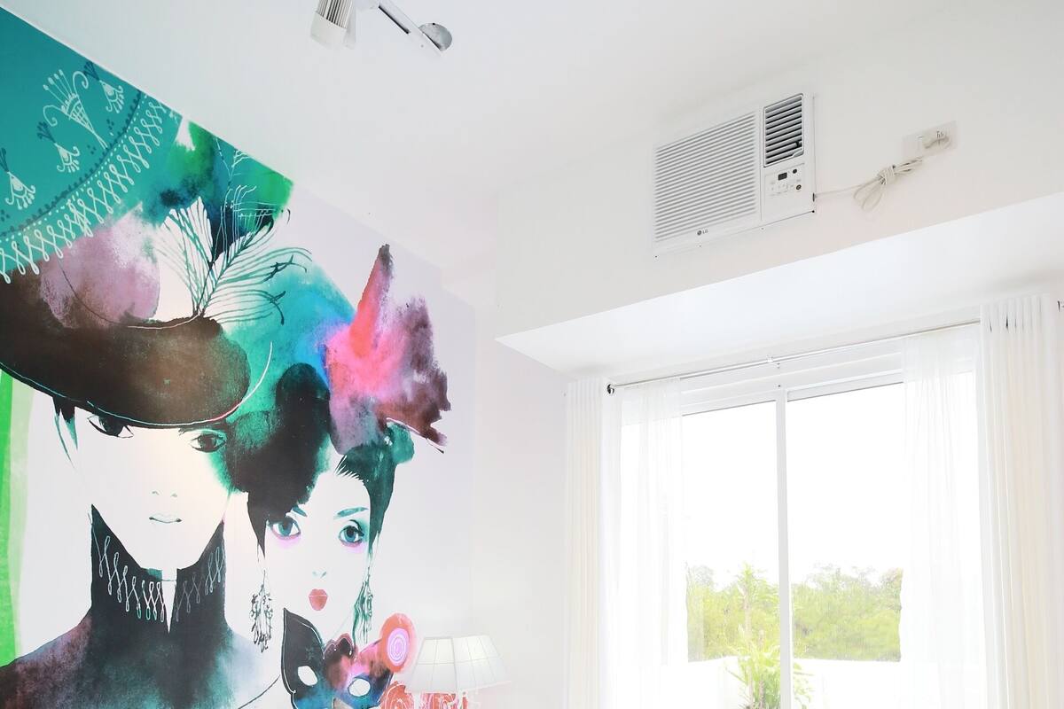 Una habitación de hotel moderna con una cama grande, un tapete verde, un cuadro en la pared y vistas por la ventana.