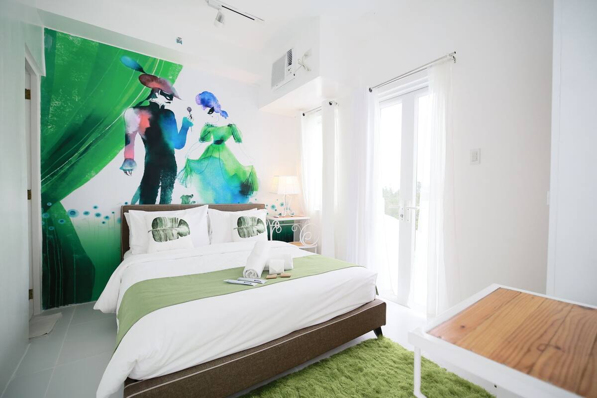 Un dormitorio moderno con una cama grande, una alfombra verde, una mesita de noche de madera y un cuadro abstracto y colorido en la pared.