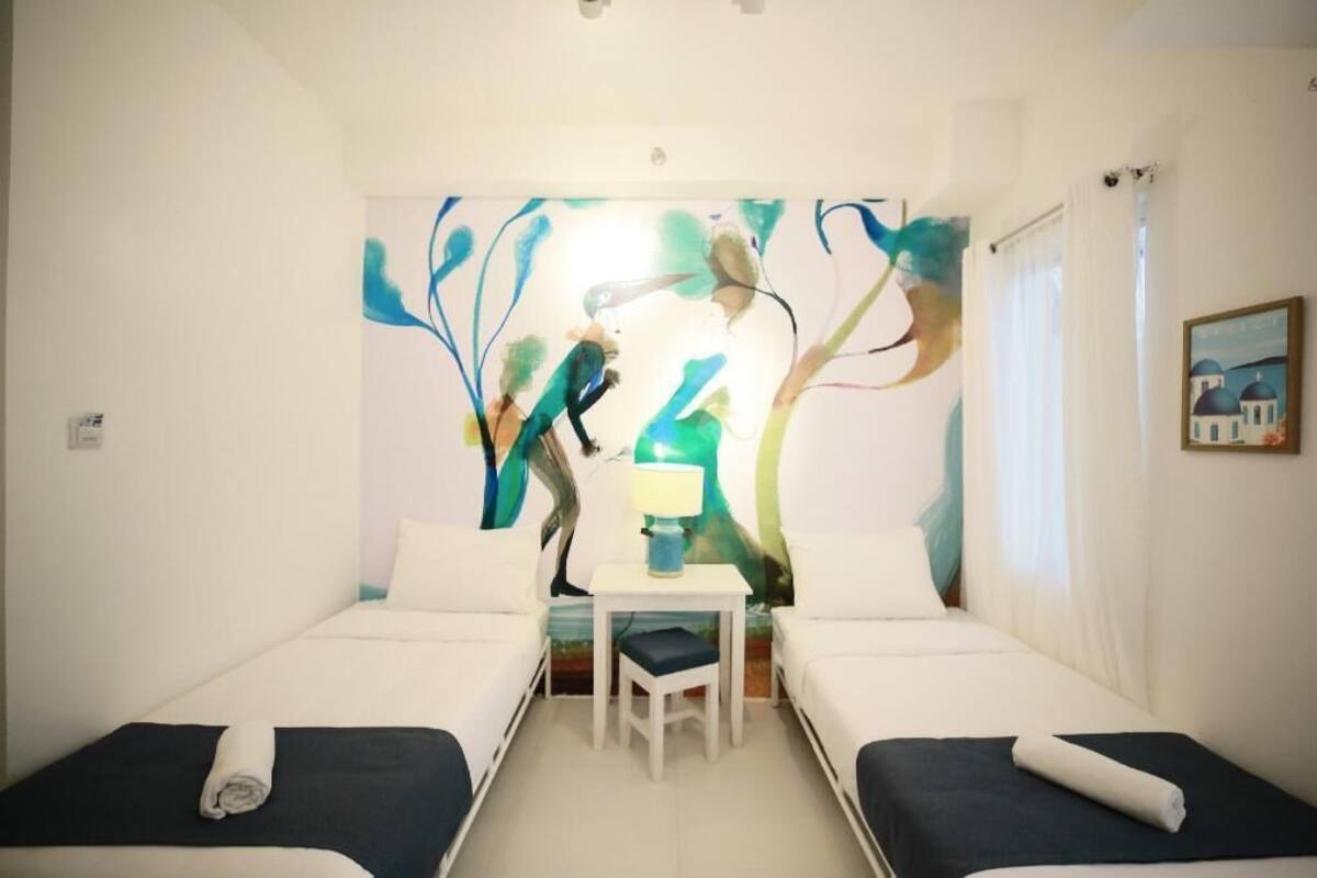 Quarto com duas camas, uma mesa pequena e uma pintura abstrata colorida na parede.
