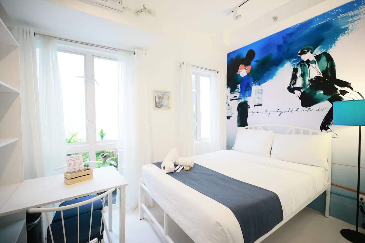 Een hotelkamer met een bed, een bureau, een stoel, een nachtkastje, een lamp en een groot raam.