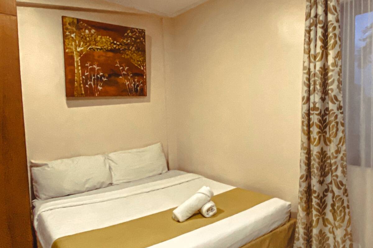 Una habitación de hotel con cama, un cuadro en la pared y una ventana con cortinas.