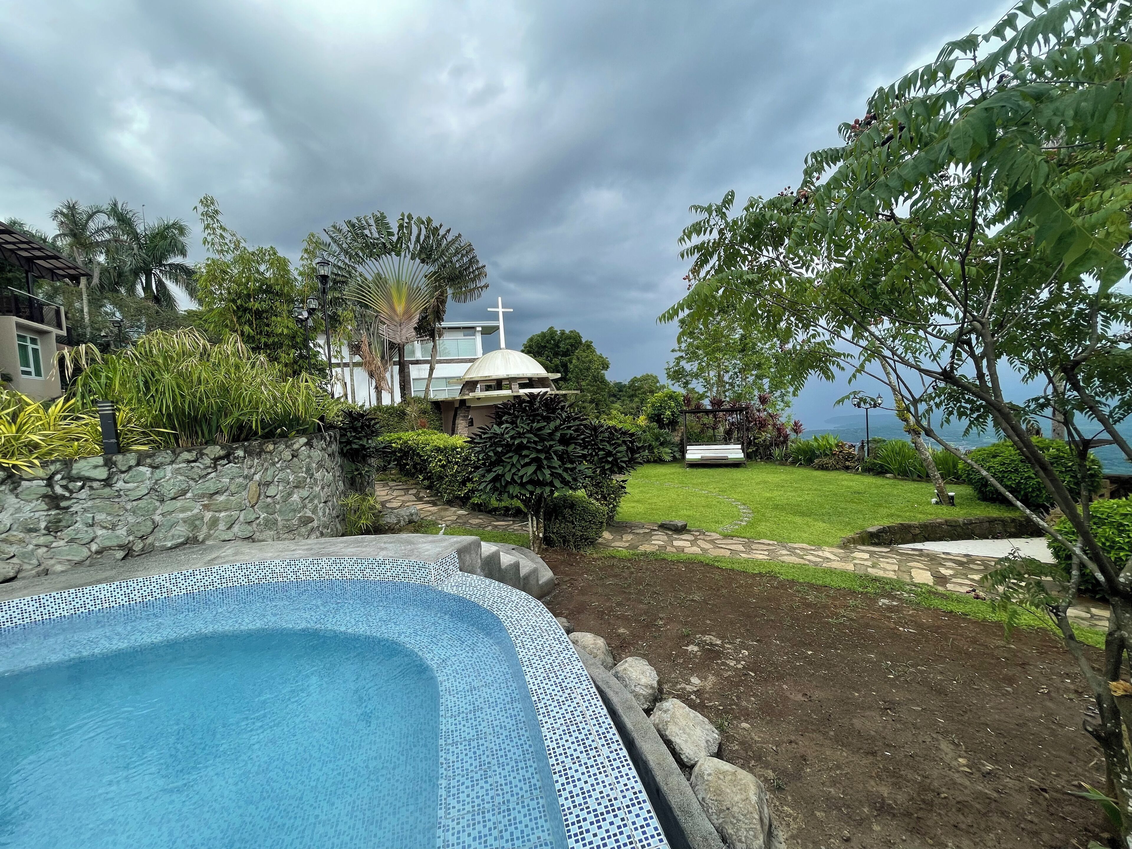 A swimming pool with a stone wall and a grassy area with a bench and a gazebo.