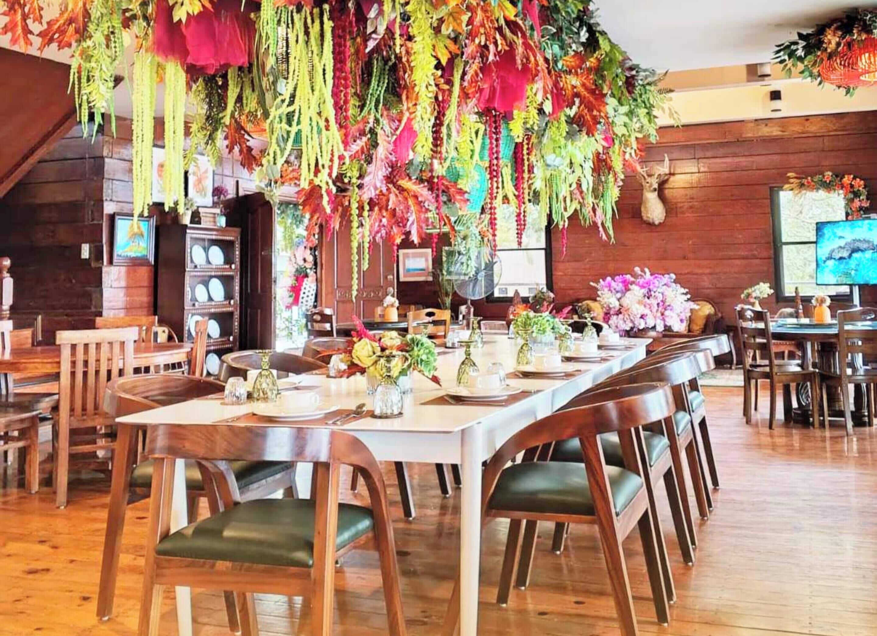 Un comedor con mesas y sillas de madera, decoraciones colgantes y una pantalla de televisión.
