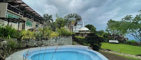 A swimming pool surrounded by lush greenery and a modern building with a cross on top.