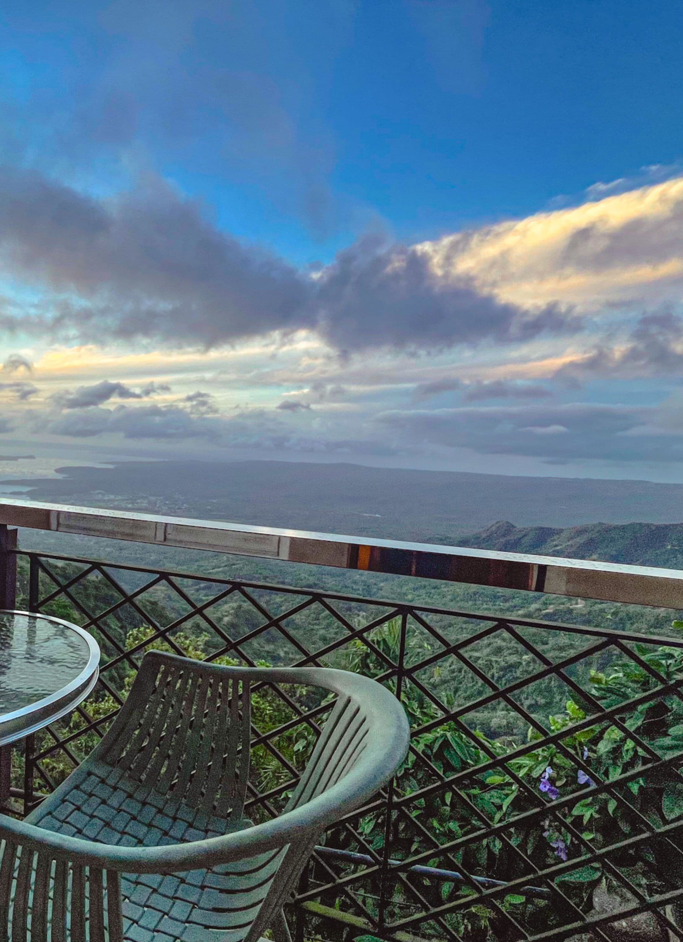 A terrace with a table and chairs, overlooking a scenic landscape with mountains and a body of water.