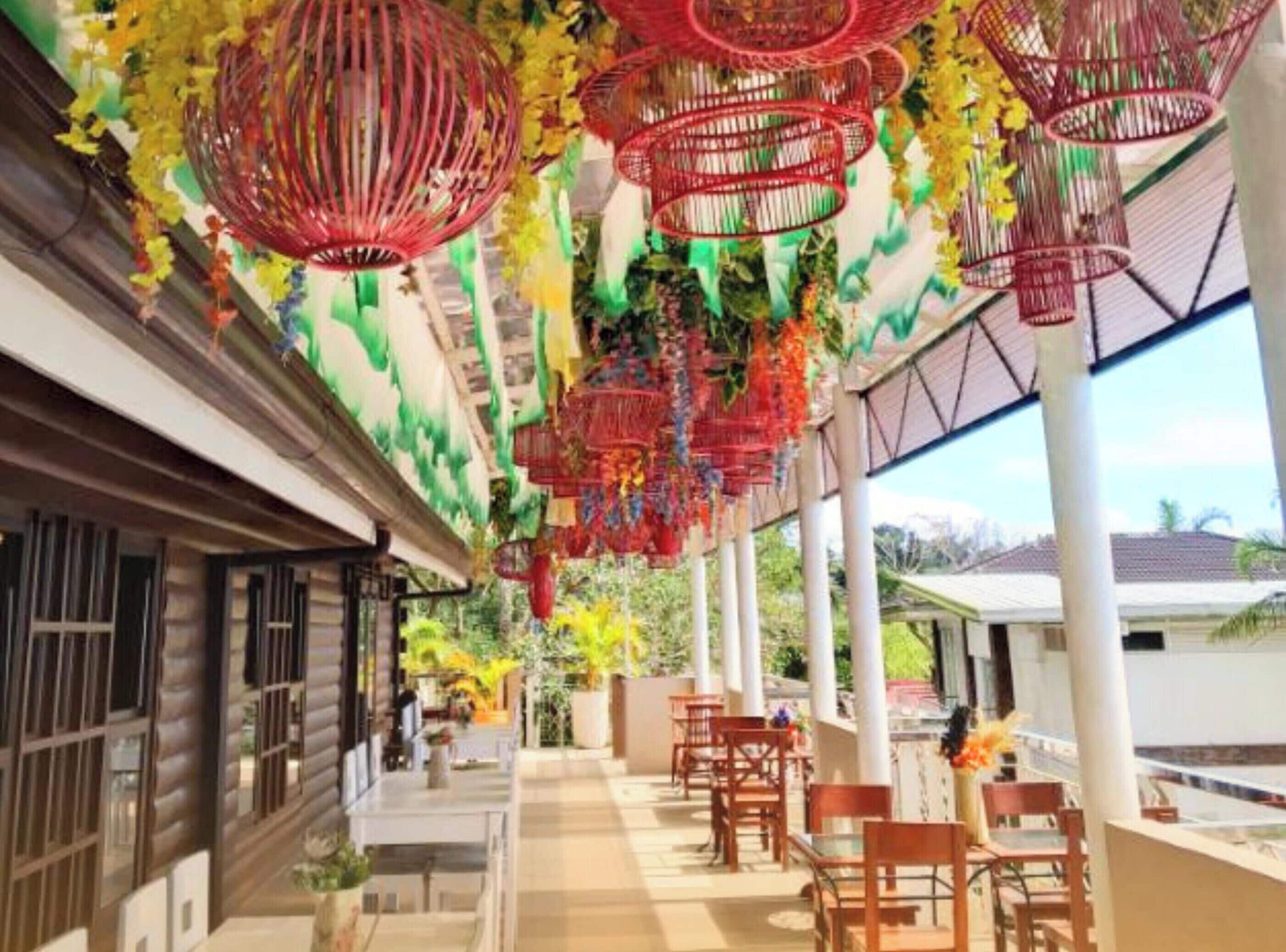 A covered outdoor area with tables and chairs, decorative hanging elements, and a building facade.