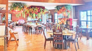 Een restaurant met houten vloeren, tafels, stoelen en hangende bloemversiering.