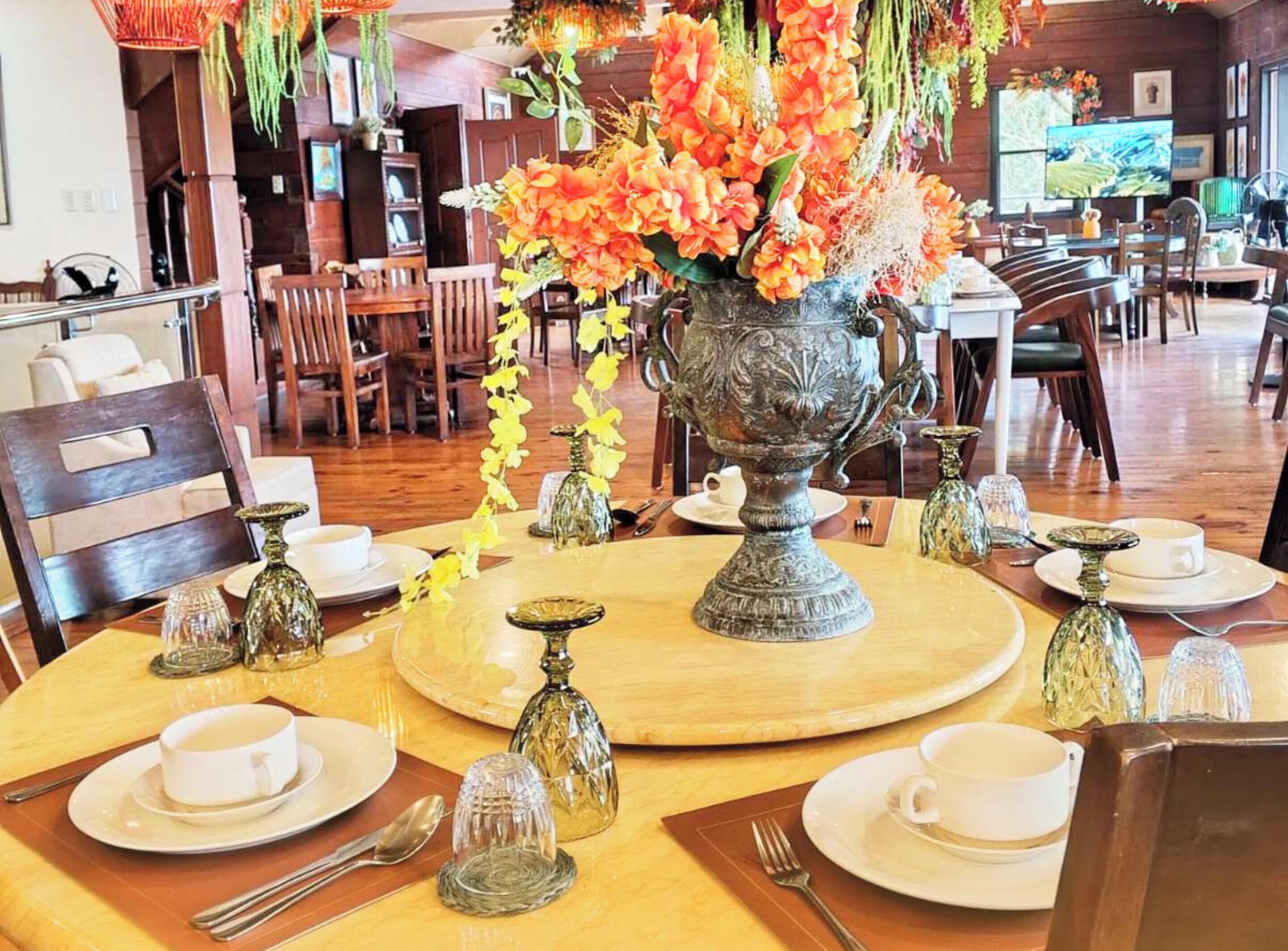 Un comedor con mesas redondas, sillas y un gran jarrón ornamentado con flores.