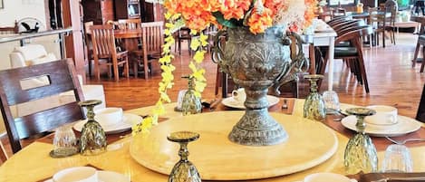 Un comedor con mesas redondas, sillas y un gran jarrón ornamentado con flores.