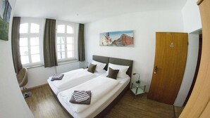Habitación de hotel con dos camas, una silla, un cuadro y una puerta.