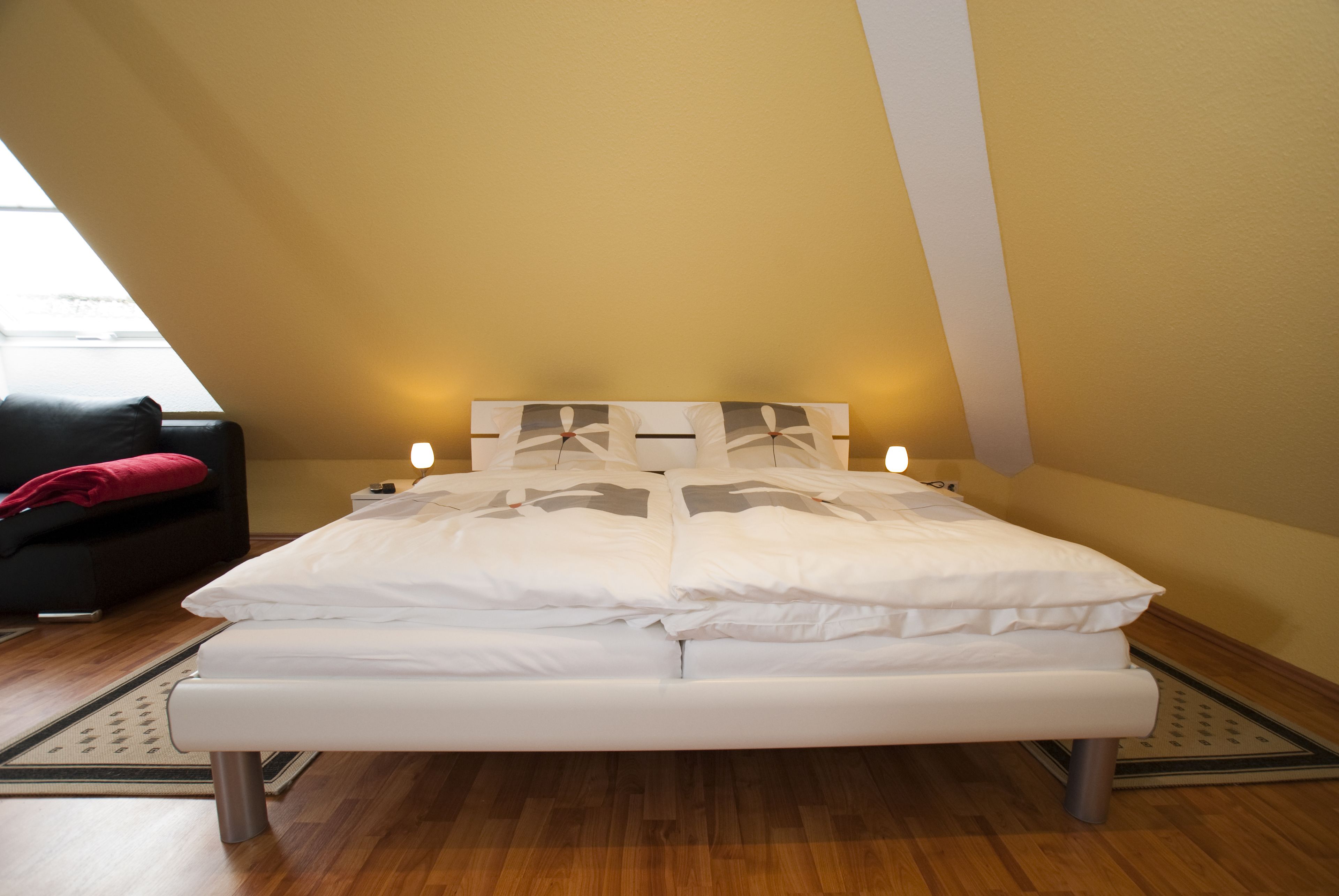 A bedroom with a bed, a nightstand, a lamp, and a window.