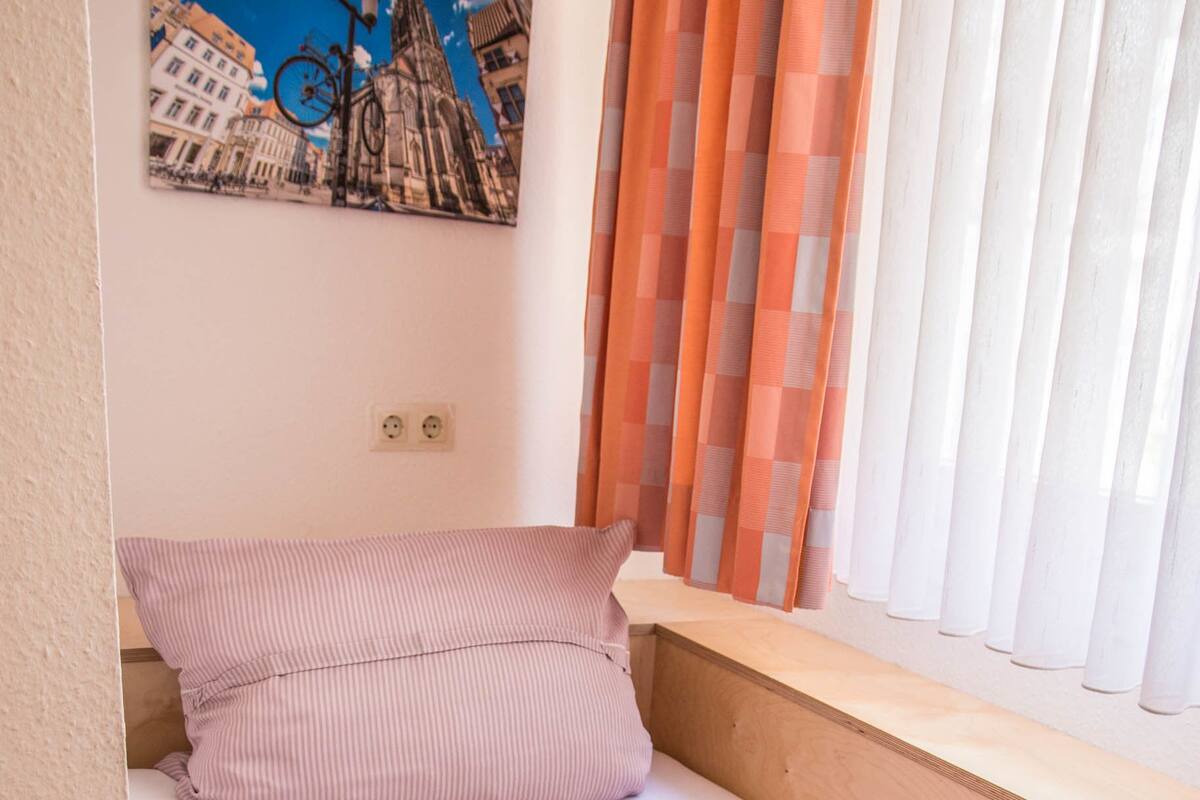 Una cama individual con ropa de cama a rayas, una almohada y una ventana con cortinas.