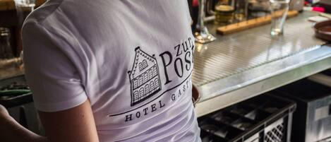 A person wearing a white t-shirt with a hotel logo and the text "HOTEL GAST" visible on the back.